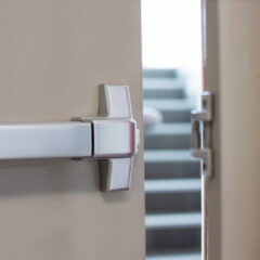 A close-up of a partially open door with a push bar, revealing a staircase in the background.